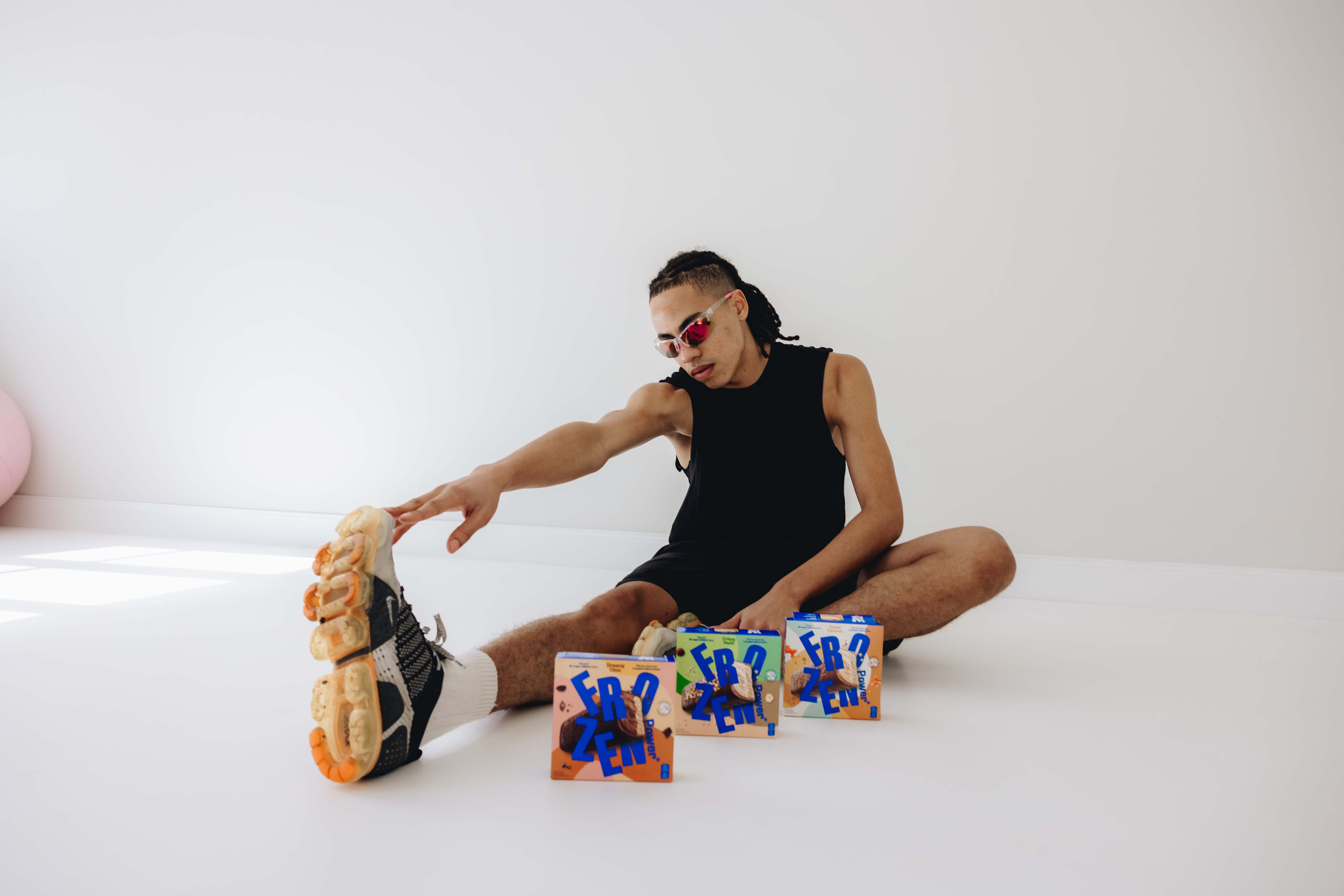 Ein Mann in sportlicher Kleidung dehnt sich, während vor ihm drei Packungen Protein-Eisriegel aufgestellt sind. Der Fokus liegt auf Fitness und gesunden Snacks für sportliche Ernährung