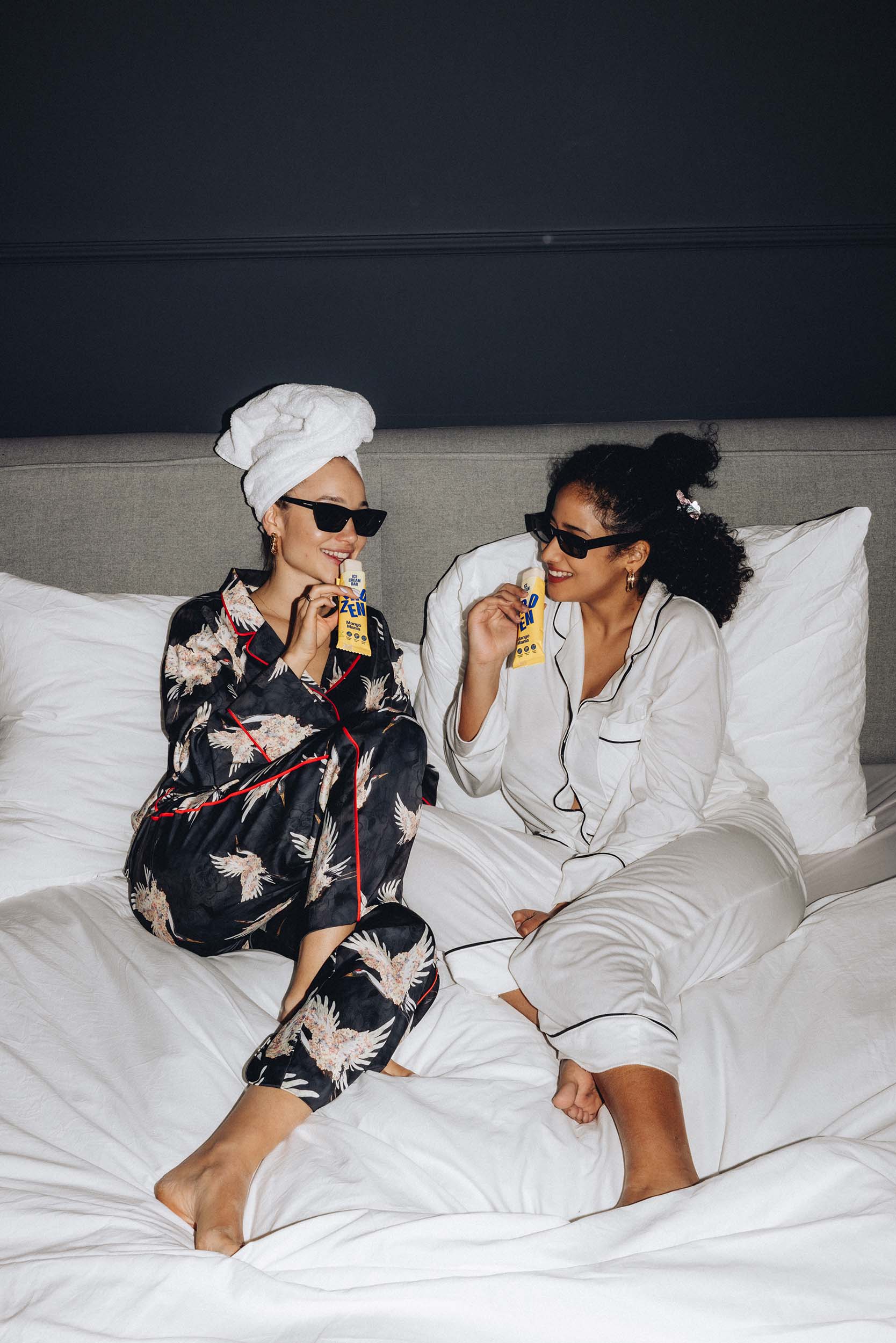 Zwei Frauen in Pyjamas sitzen auf einem Bett und genießen den Frozen Power Mango Mania Protein Eis-Riegel ohne Zuckerzusatz von Frozen Power