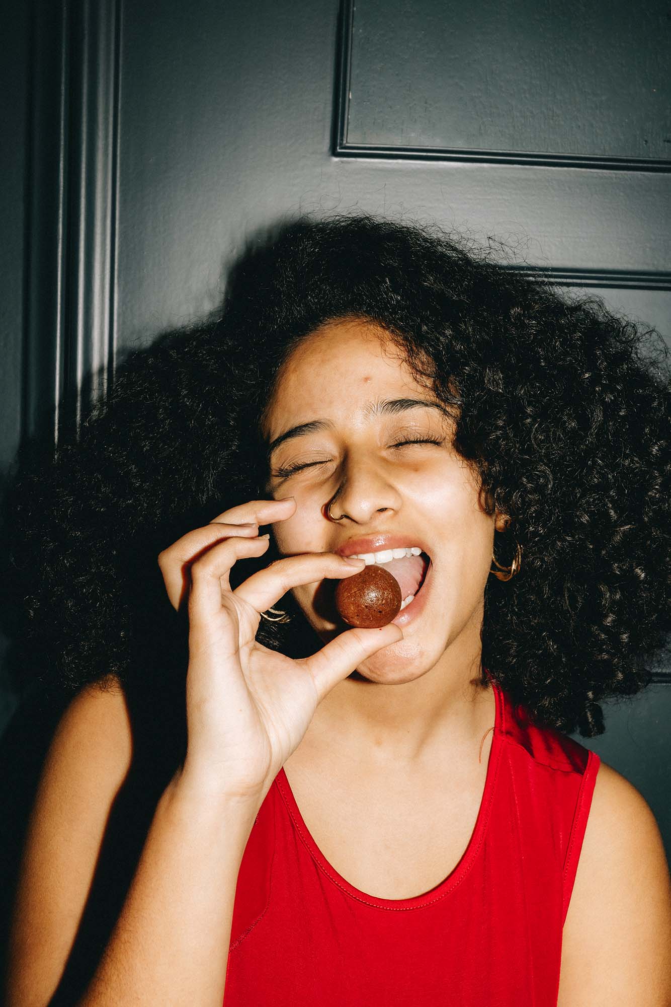 Eine Frau in rotem Oberteil genießt ein veganes Zuckerfreies Dattel Energie Bällchen mit Himbeereis Füllung von Frozen Power