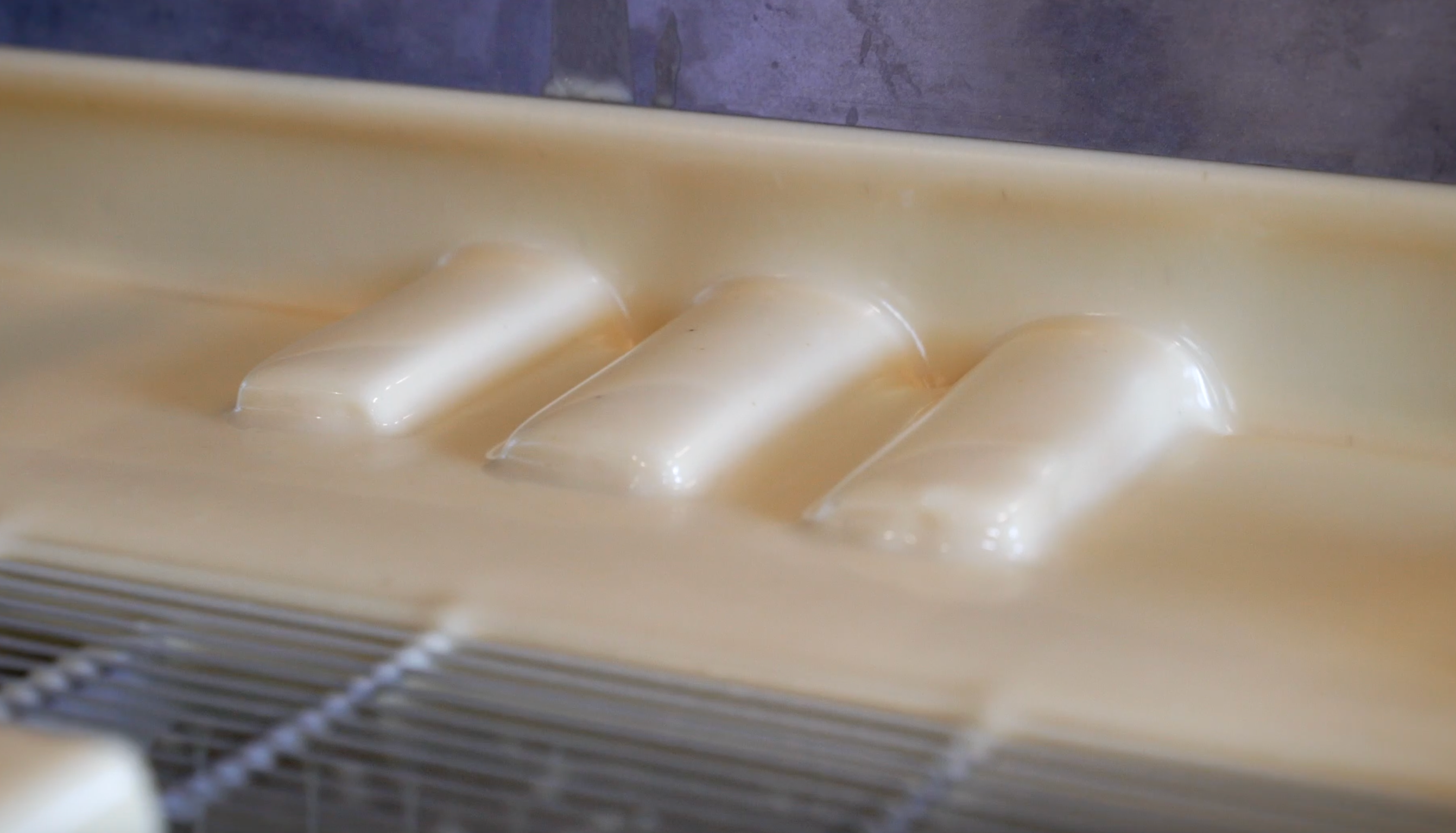 Drei Protein-Eisriegel in einer Produktionsphase, umhüllt von einer cremig-weißen Glasur. Der Fokus liegt auf der glatten Oberfläche der Riegel, die in der Herstellung verarbeitet werden, passend für eine kalorienarme und proteinreiche Ernährung. Ideal für zuckerfreie Fitness-Snacks und proteinreiche Ernährung.
